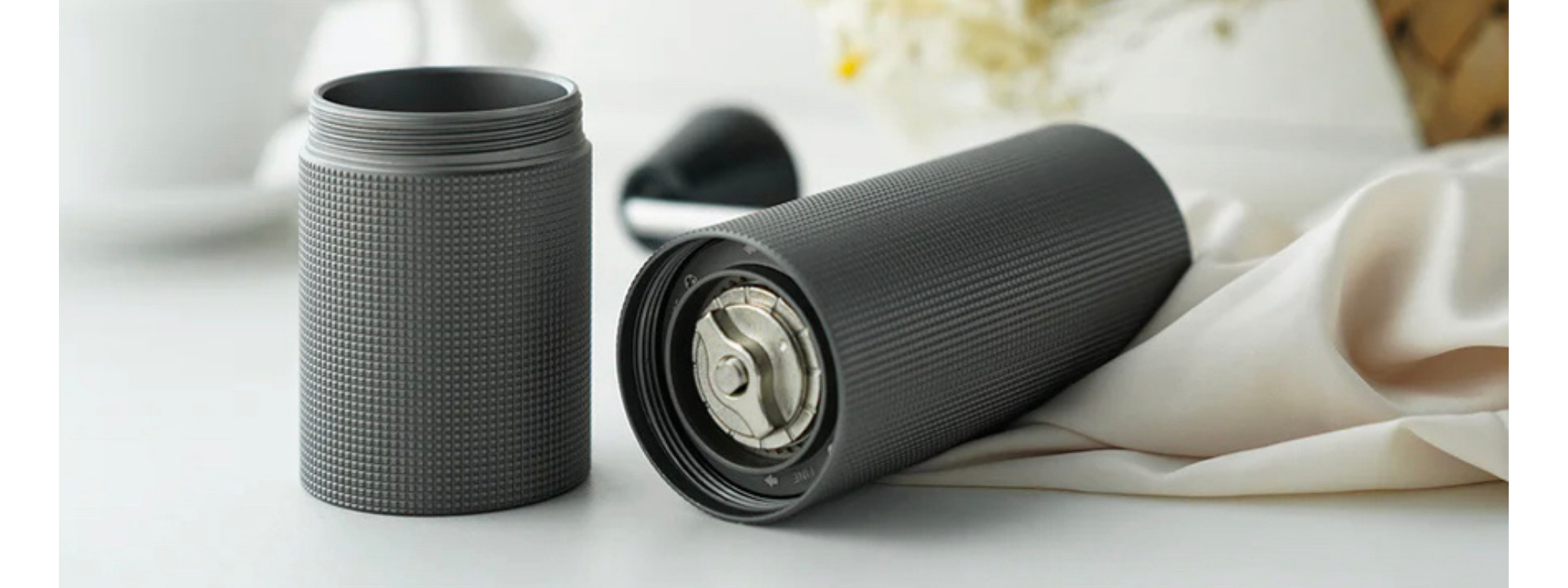 Imagem do moedor de café Timemore c2 na cor cinza sobre uma mesa branca com detalhe de flores nos cantos