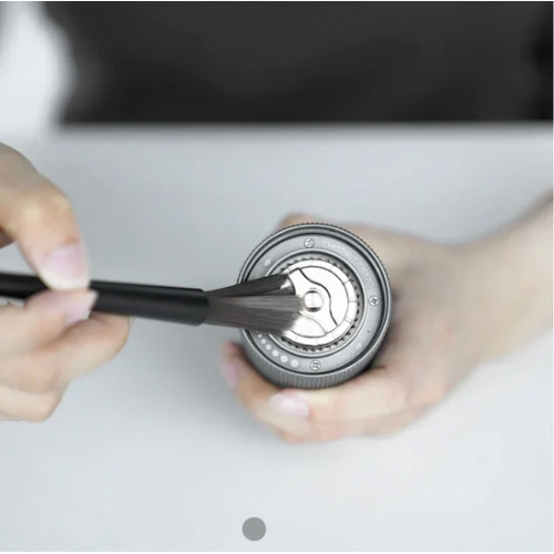 Imagem de mãos de pessoa branca, segurando o moedor de café e passando pincel de limpeza no fundo da peça em uma mesa branca